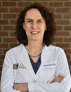 Dr. Rebecca Baxt in a lab coat, arms folded in front of a brick wall